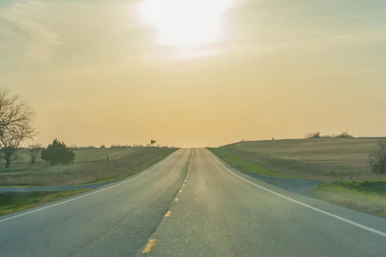 An open country road stretching ahead under a soft golden sky.
